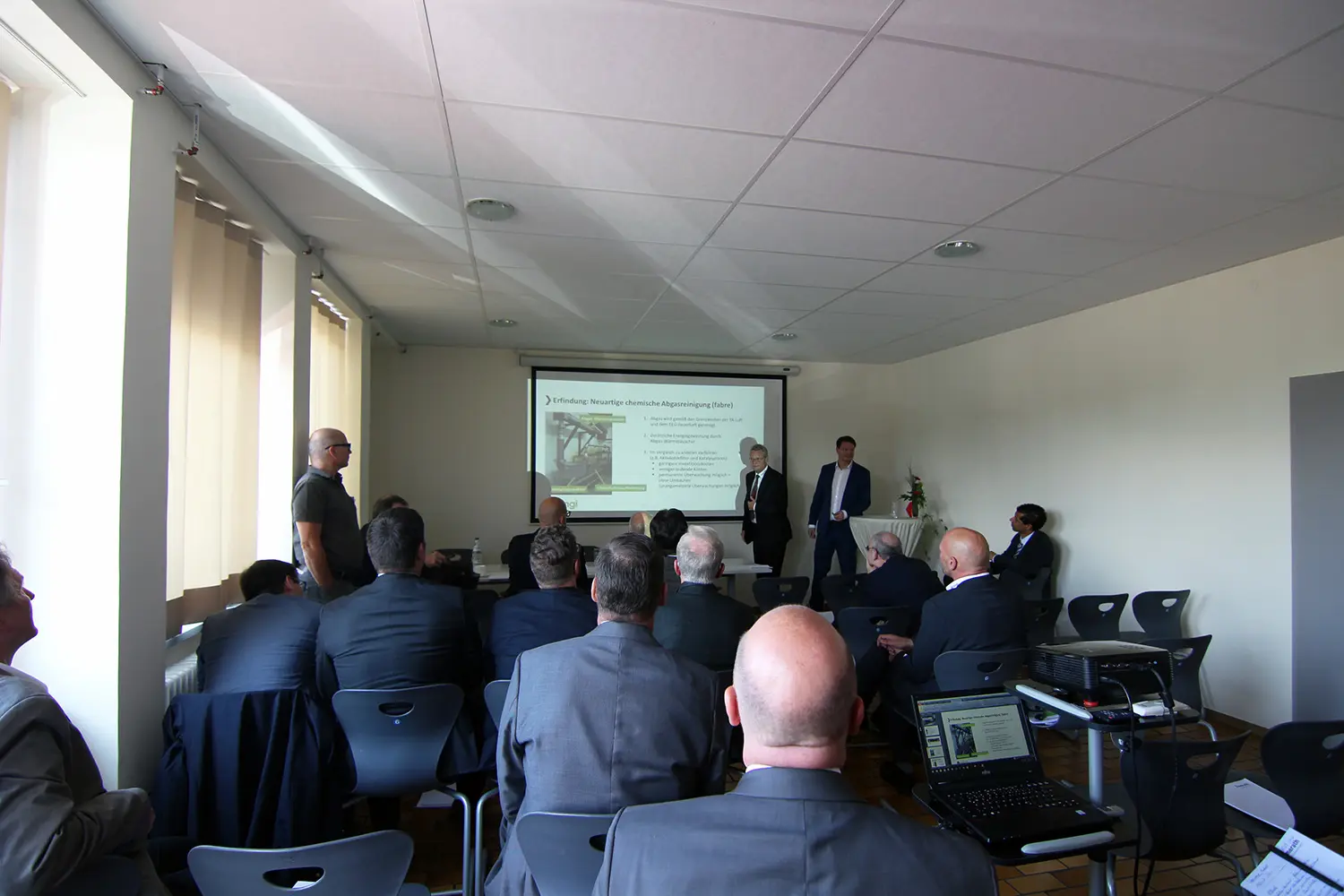 Publikum in einem Konferenzraum bei einem Vortrag mit Präsentation an der Leinwand