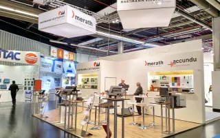 Messestand von merath, accundu und Hartmann Electronic auf der Embedded World 2018 mit Parkettboden, Stehtischen und weißer Rückwand mit Logoaufdrucken