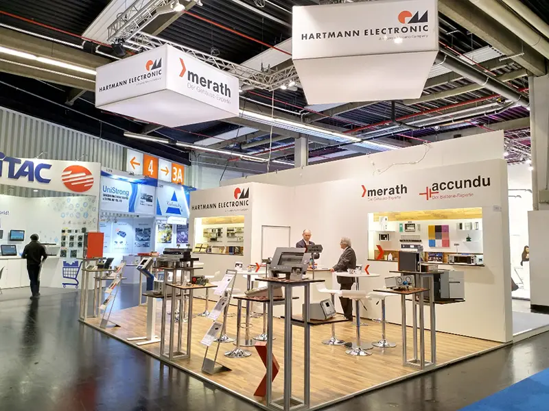 embedded-world-2018_merath_accundu_hartmann Messestand von merath, accundu und Hartmann Electronic auf der Embedded World 2018 mit Parkettboden, Stehtischen und weißer Rückwand mit Logoaufdrucken