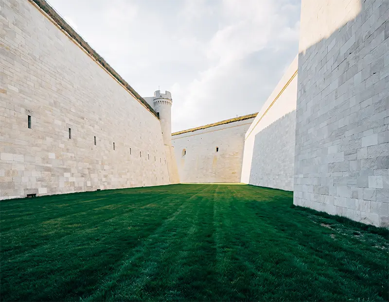 Innenhof einer Festungsanlage mit hohen, hellen Steinmauern und gepflegter Grünfläche
