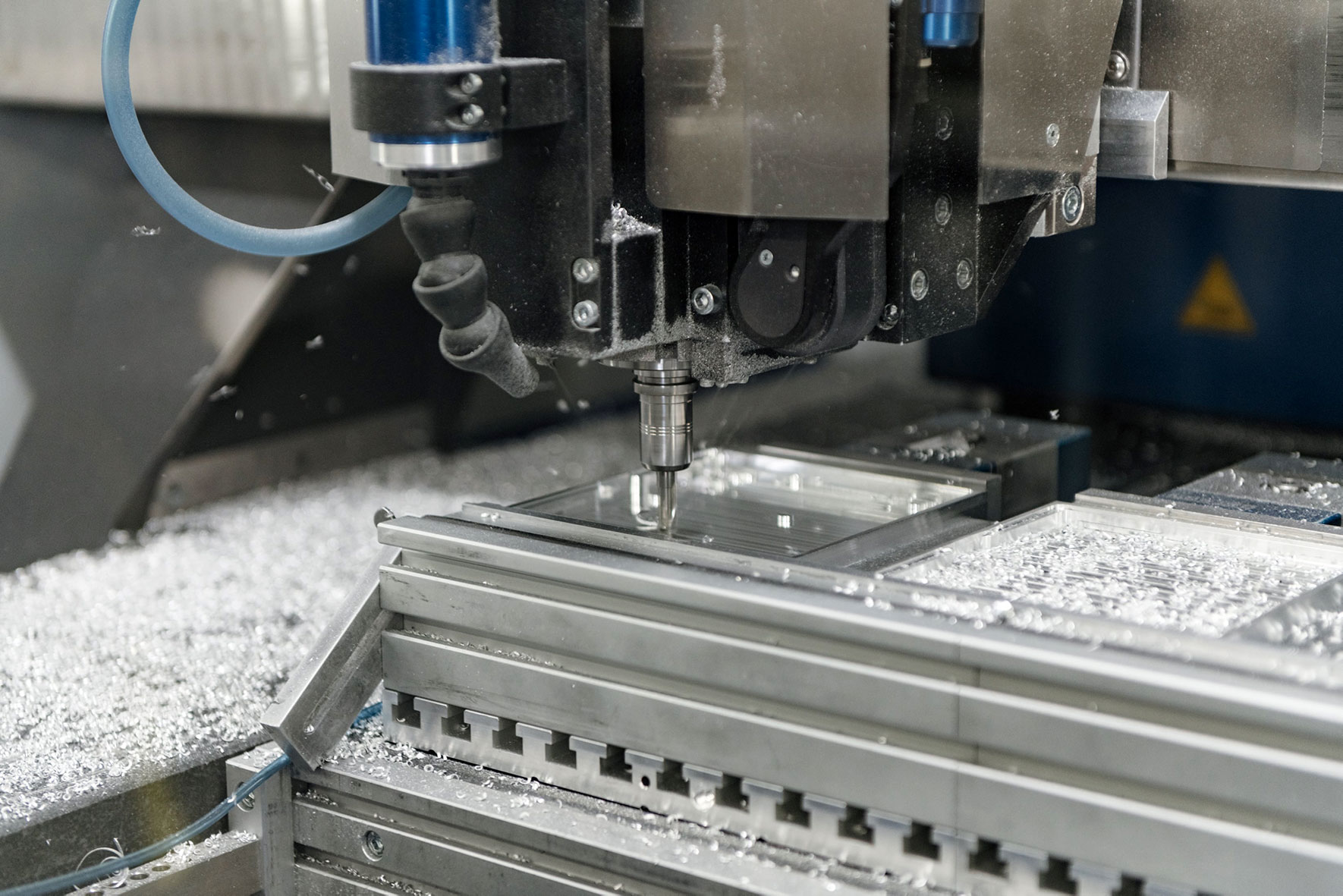 Nahaufnahme des Fräskopfes einer CNC-Fräse bei der Bearbeitung eines quadratischen Aluminiumteils.