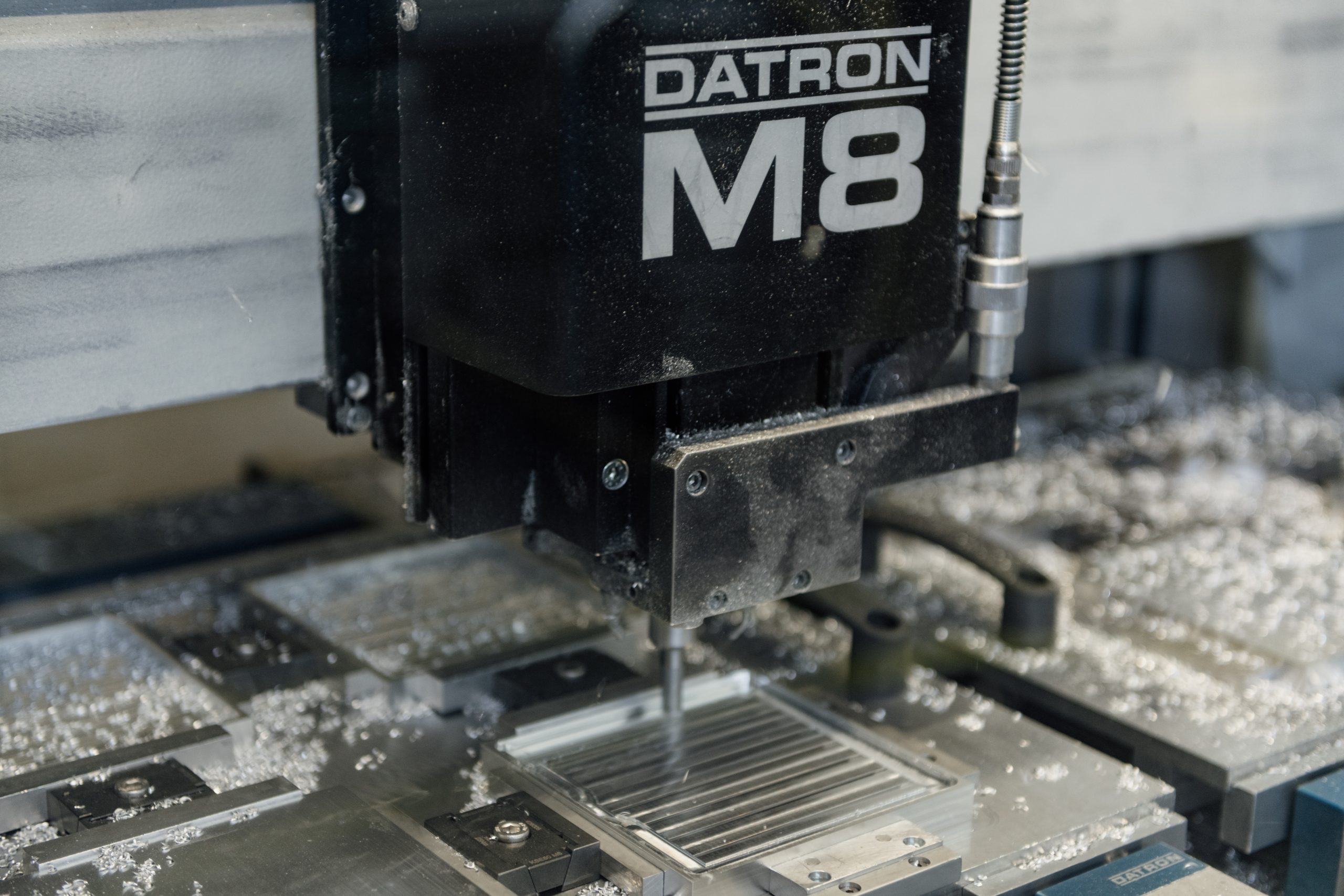 Fräskopf einer Datron CNC-Fräsmaschine mit Aufschrift "DATRON M8" bei der Bearbeitung eines Aluminium-Blocks.