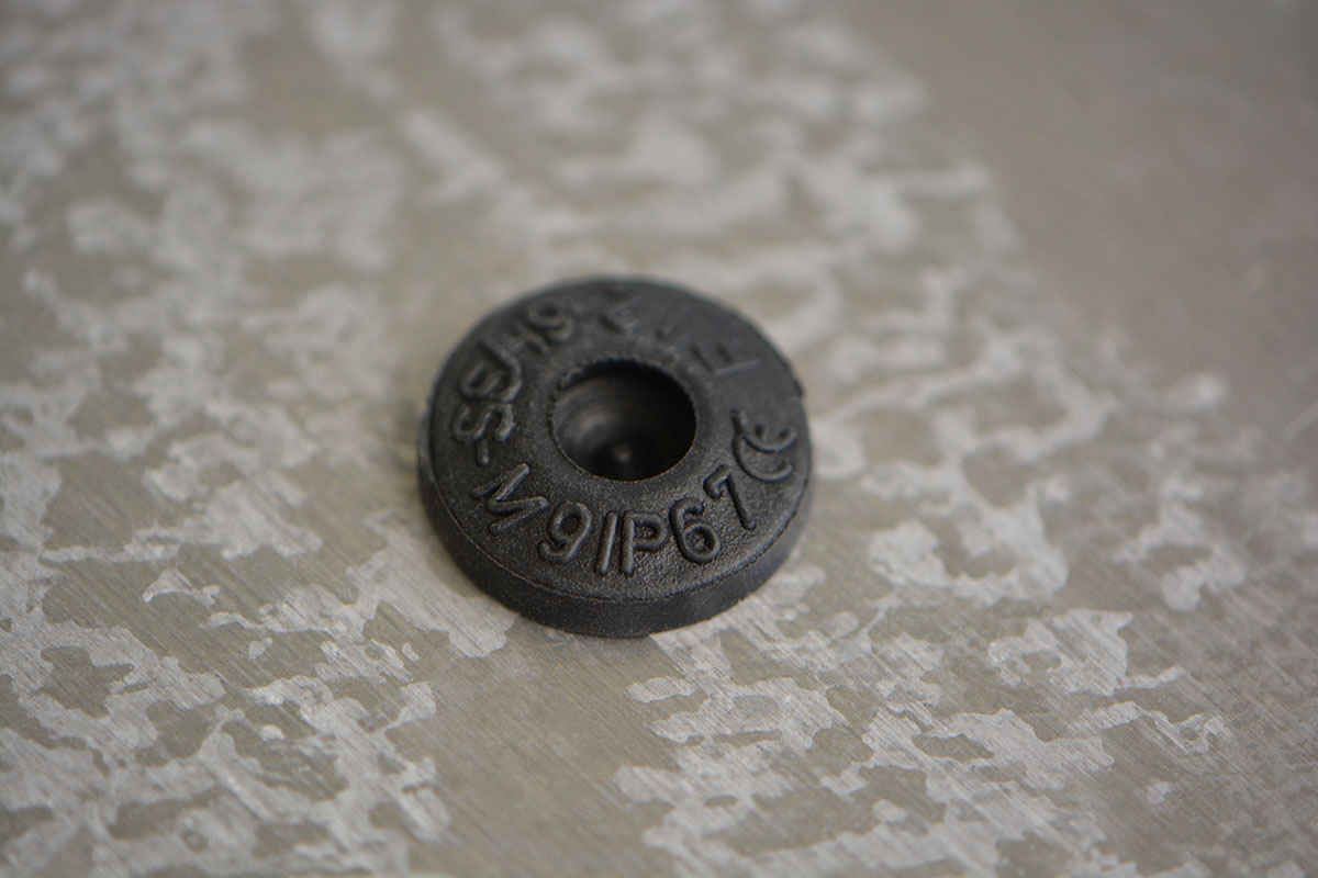 Kleine, runde Dichtungstülle aus schwarzem Kunststoff mit Aufschrift: "M9IP67"