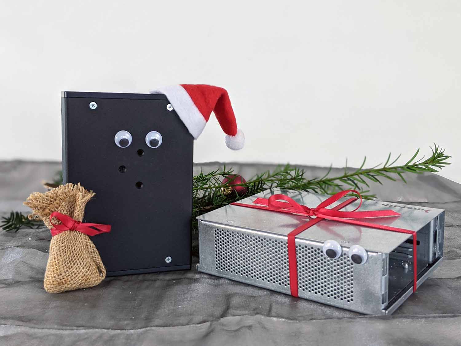 Ein schwarzes Gehäuse mit Kulleraugen und Weihnachtsmannmütze und ein silbernes Gehäuse mit Kulleraugen und Geschenkband