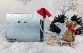 Ein Metallgehäuse mit Nikolausmütze zieht einen kleinen Schlitten, auf dem ein Säckchen steht durch eine Winterlandschaft.