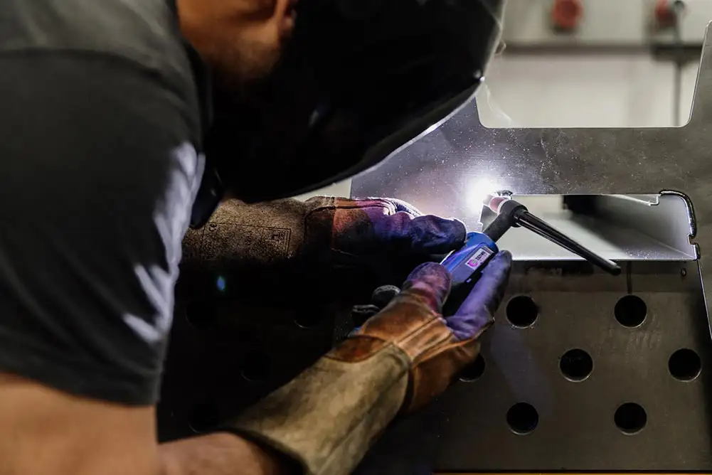 Mitarbeiter mit Schweißermaske schweißt ein Bauteil aus Stahl mit einem Handschweißgerät