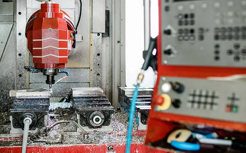 CNC-Fräsmaschine mit rotem Fräskopf, Werkstückspannern und Bedienpult im Vordergrund